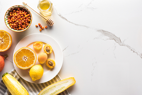 top view of plate with orange, apricots, lemon, zucchini6 berries and honey on marble surface