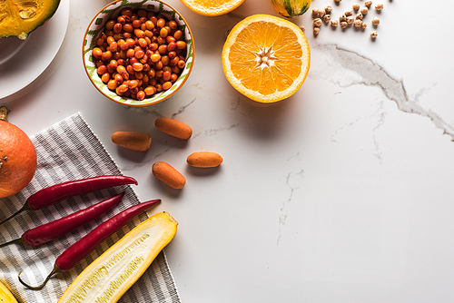 top view of orange, bowl with berries and chili peppers on marble surface