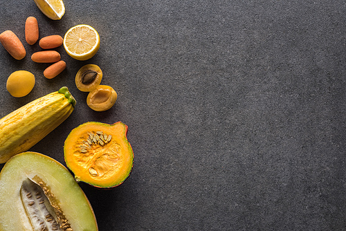 top view of yellow fruits and vegetables on grey textured background with copy space