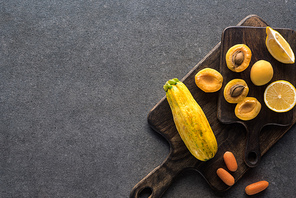 top view of yellow fruits and vegetables on wooden cutting boards on grey textured background with copy space