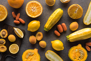 top view of yellow fruits and vegetables on wooden cutting board on grey textured background