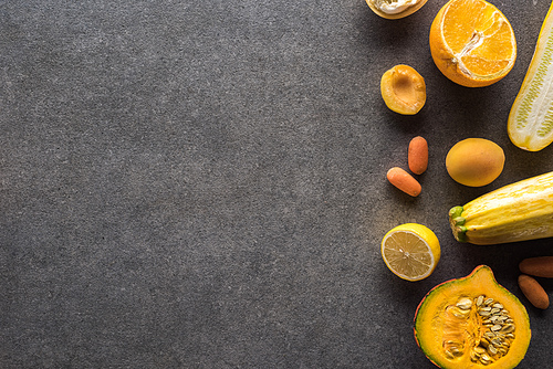 top view of yellow fruits and vegetables on grey textured background with copy space