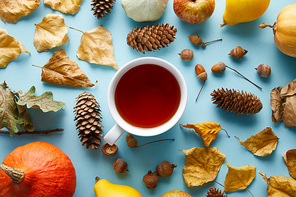 top view of mug with tea near autumnal decoration on blue background