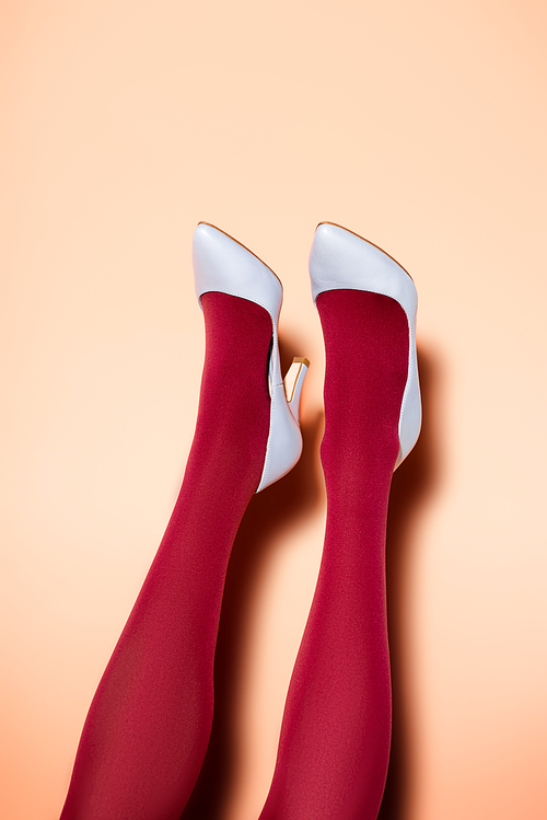 cropped view of female legs in red tights and blue shoes on peach background