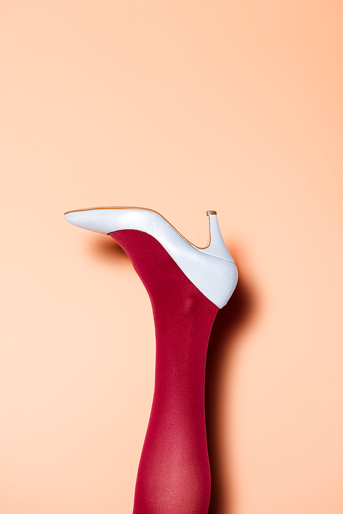 cropped view of female leg in red tights and blue shoes on peach background