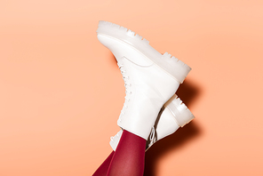cropped view of female legs in red tights and white boots on peach background