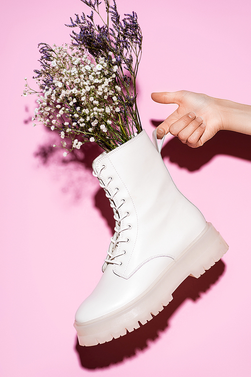 cropped view of woman holding white boot with wildflowers on pink background