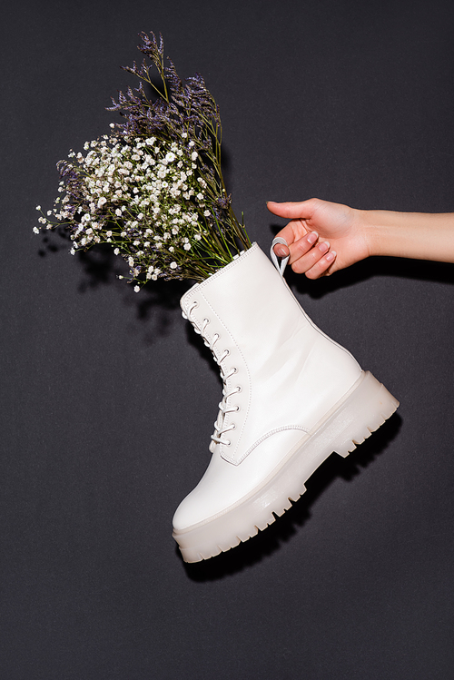 cropped view of woman holding white boot with wildflowers on black background