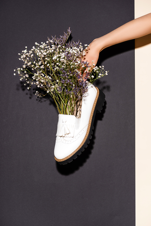 cropped view of woman holding white shoe with wildflowers on black background
