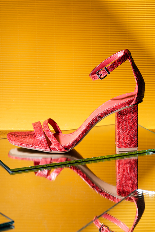 elegant pink snakeskin heeled sandals on mirror surface on yellow background