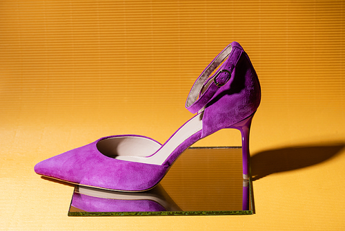 elegant violet suede heeled shoe on mirror on yellow background