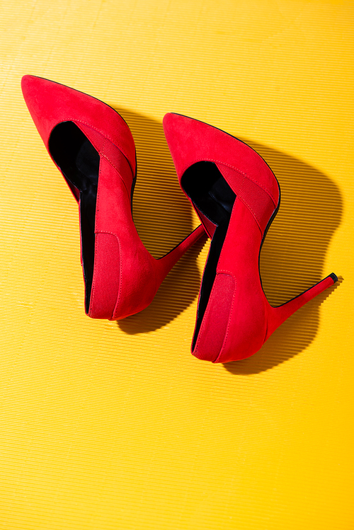 top view of elegant red suede heeled shoes on yellow background