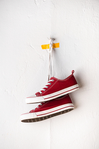 casual red sneakers hanging on shoelaces near white textured wall