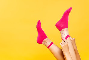Cropped view of woman putting pink socks on legs isolated on yellow