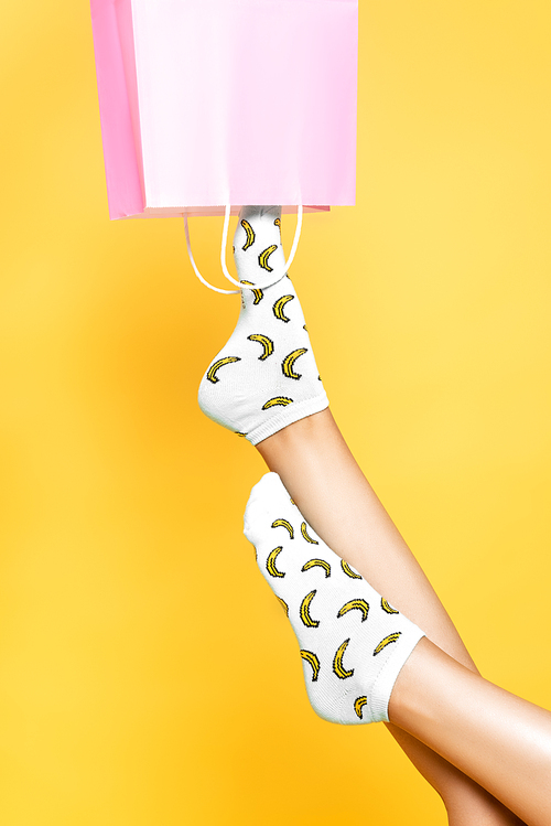 Cropped view of woman wearing socks, putting leg in pink paper bag isolated on yellow background