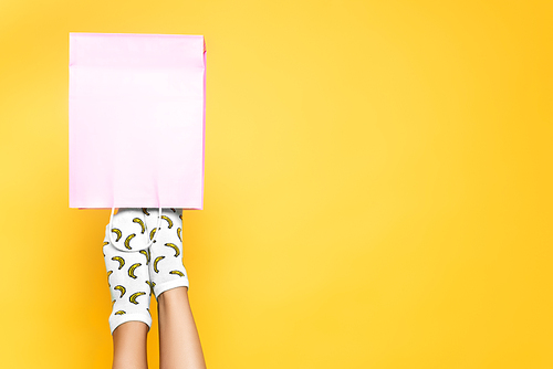 Top view of woman with socks putting feet in pink paper bag isolated on yellow background
