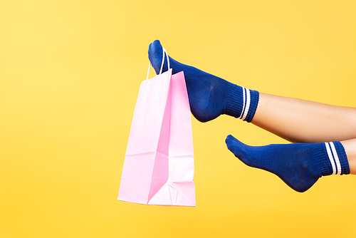 Cropped view of pink paper bag hanging on woman leg in socks isolated on yellow background