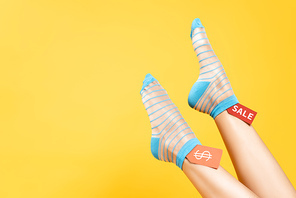 Cropped view of female legs in socks and tags with dollar symbol and sale word isolated on yellow