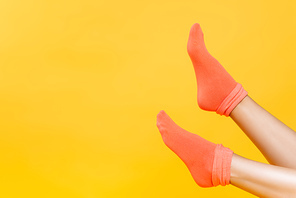 Cropped view of female legs in soft orange socks isolated on yellow