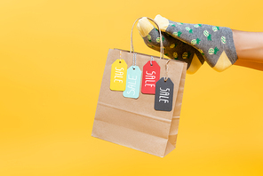 Cropped view of paper bag with sale tags hanging on woman leg in socks isolated on yellow