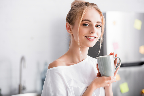 joyful blonde woman  while standing in kitchen with cup of tea