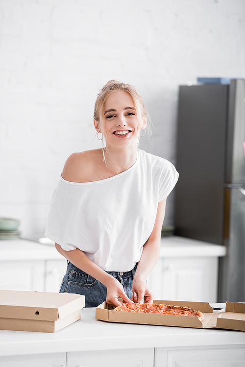 joyful woman  while taking pizza from box in kitchen