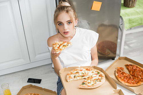 high angle view of young woman sitting of floor in kitchen with piece of pizza