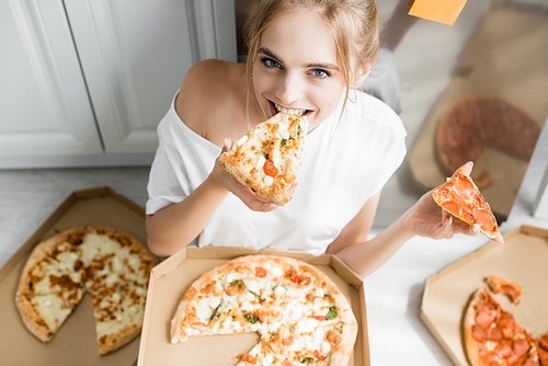 high angle view of blonde woman eating pizza while sitting on floor in kitchen