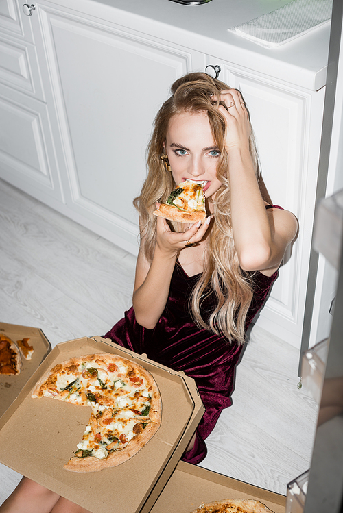 high angle view of sexy woman eating pizza and touching hair while sitting on floor and 