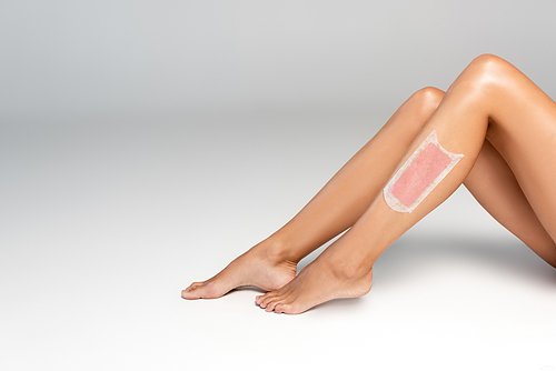 Cropped view of woman smooth legs with pink wax stripe on grey