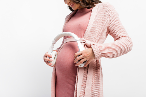 cropped view of pregnant woman holding wireless headphones near belly isolated on white