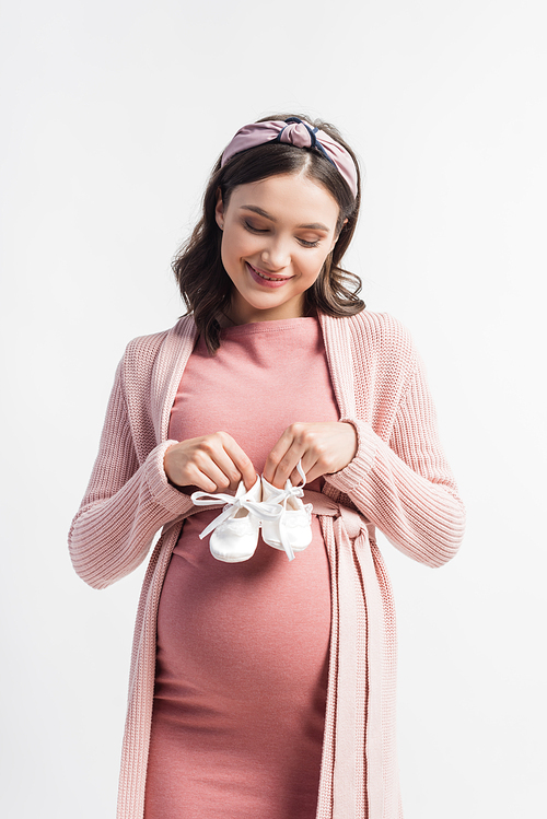 joyful and pregnant woman holding tiny boots isolated on white