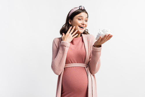 pleased and pregnant woman looking at tiny boots isolated on white