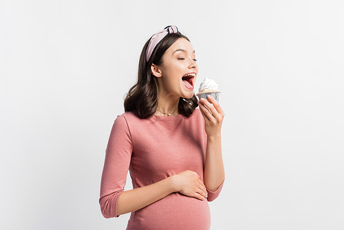 joyful pregnant woman with open mouth holding cupcake isolated on white