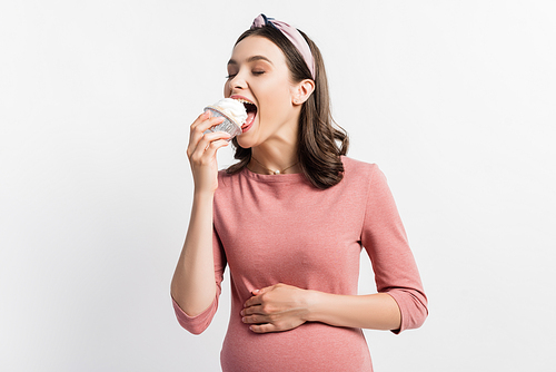 joyful pregnant woman with closed eyes eating cupcake isolated on white