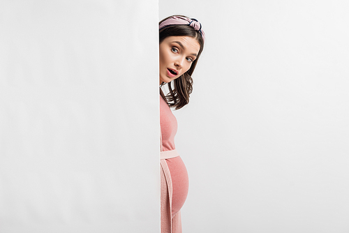 shocked and pregnant woman hiding near wall isolated on white