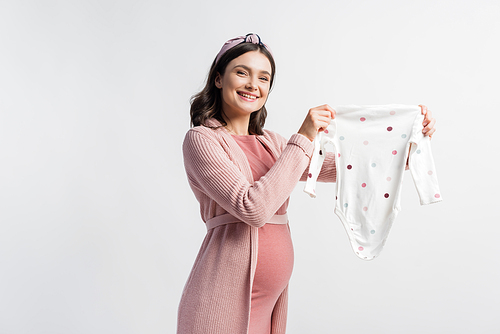 pleased pregnant woman in headband holding baby romper isolated on white