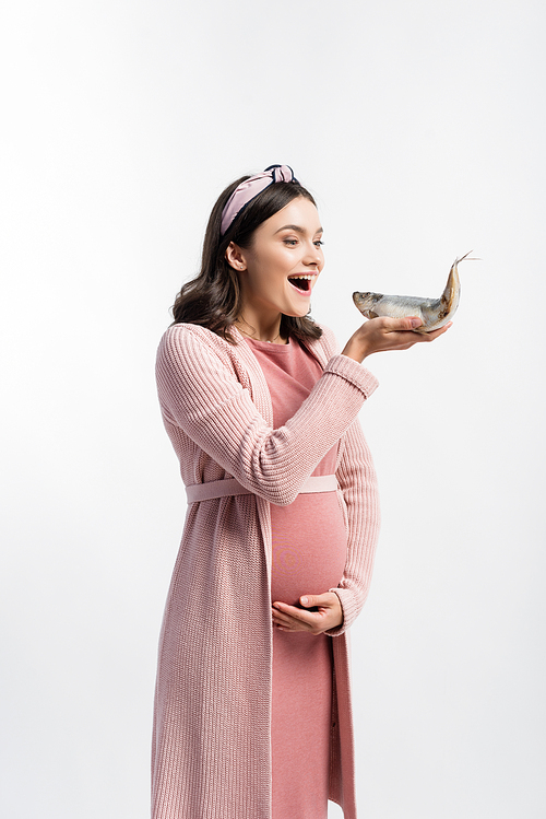 pregnant woman with open mouth looking at dried fish and touching belly isolated on white