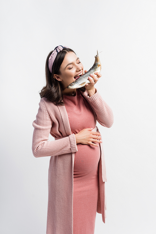 pregnant woman with closed eyes and open mouth eating dried fish isolated on white