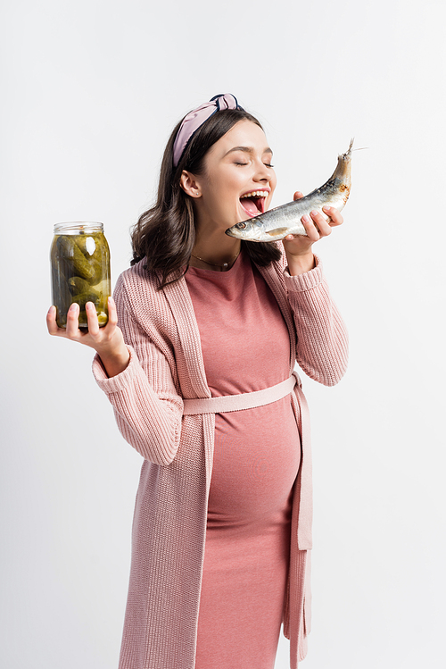 pregnant woman with open mouth holding jar with pickled cucumbers and dried fish isolated on white