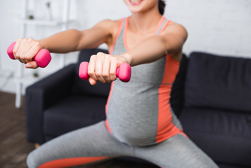 selective focus of pregnant woman exercising with pink dumbbells at home