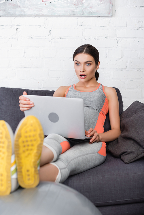 selective focus of shocked and pregnant woman looking at laptop in living room