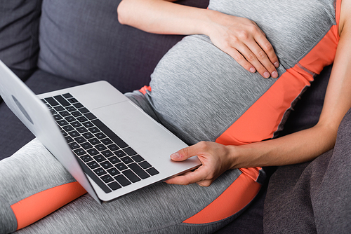 partial view of pregnant woman in sportswear using laptop at home