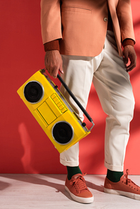 cropped view of stylish man holding boombox on red with shadows