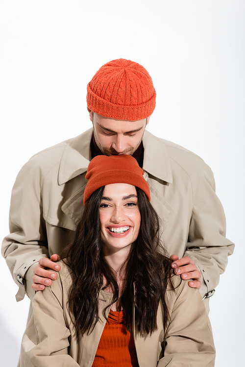 man in beanie hat kissing head of joyful woman isolated on white