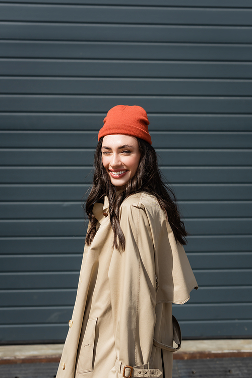 joyful woman in trench coat and beanie hat winking eye