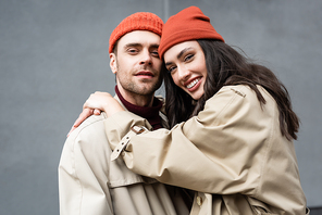 trendy woman in beanie hat hugging man in trench coat