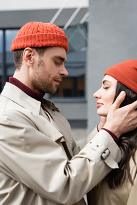 side view of trendy man touching young woman in beanie hat