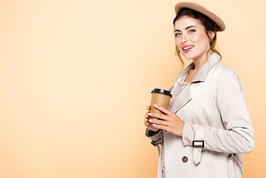 fashionable woman in autumn outfit holding coffee to go while  isolated on peach
