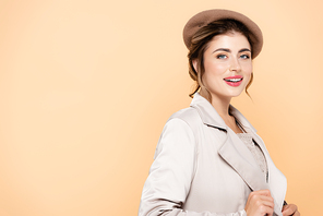 sensual woman in stylish beret and trench coat  while posing isolated on peach